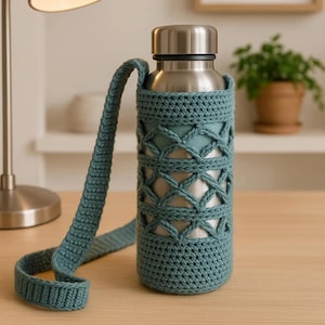 May include: A stainless steel water bottle with a teal crochet cozy and strap. The cozy features a lattice design and covers the bottle, with a matching strap for easy carrying. The bottle is on a wooden surface.