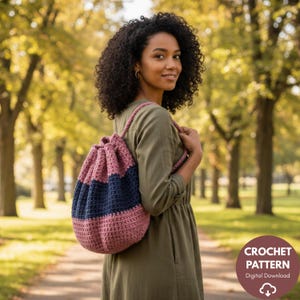 Könnte beinhalten: Ein handgefertigter Häkelrucksack in den Farben Staubrosa, Marineblau und Rosarot. Die Kordelzugtasche wird über der Schulter getragen. Das Bild enthält eine kreisförmige Grafik mit den Worten "CROCHET PATTERN" und "Digital Download".