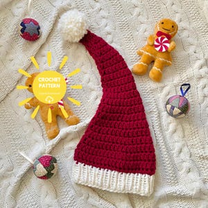 Op de afbeelding: Een rood-witte gehaakte kerstmuts met een witte pompon, twee peperkoekpop-knuffels en drie stoffen ornamenten. Een gele zonnestraalgrafiek met de tekst CROCHET PATTERN Digital Download is aan de linkerkant over de afbeelding geplaatst.