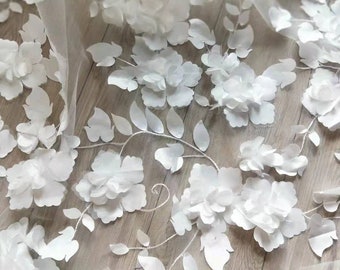 May include: White floral lace fabric with 3D flowers and leaves. The fabric has a delicate, sheer texture and is perfect for adding a touch of elegance to any project.