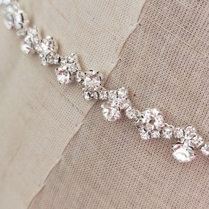 Puede incluir: Un collar plateado con un diseño delicado de pequeños diamantes de imitación transparentes dispuestos en un patrón geométrico.