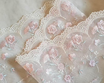 May include: Delicate floral lace trim in soft pink and white. The lace features embroidered flowers and leaves, with a scalloped edge. The fabric is sheer, creating a romantic and airy feel. Ideal for adding a touch of elegance to various craft projects.