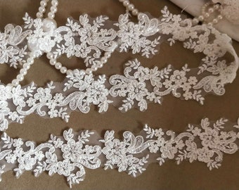 Puede incluir: Borde de encaje blanco con un diseño floral y pequeñas lentejuelas. El borde es delicado e intrincado, perfecto para agregar un toque de elegancia a cualquier proyecto.