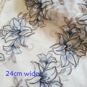 May include: A white sheer fabric with embroidered gray and blue lilies. The fabric is 24 inches wide.