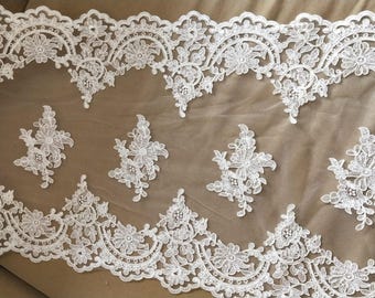 Könnte beinhalten: Weiße Spitzenborte mit einem zarten Blumenmuster. Die Spitze hat einen gewellten Rand und ist perfekt, um jedem Projekt einen Hauch von Eleganz zu verleihen.