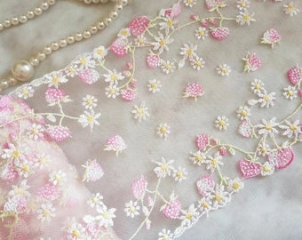 Puede incluir: Primer plano de delicado encaje floral con flores bordadas rosas y blancas y detalles amarillos. El encaje presenta un patrón repetido de margaritas y formas similares a bayas, ideal para manualidades o adornos.