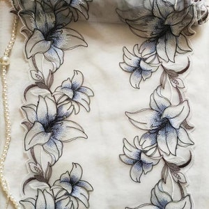 May include: White sheer fabric with embroidered blue and brown lilies. The fabric is 31 inches wide.