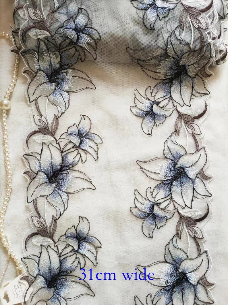 May include: White sheer fabric with embroidered blue and brown lilies. The fabric is 31 inches wide.