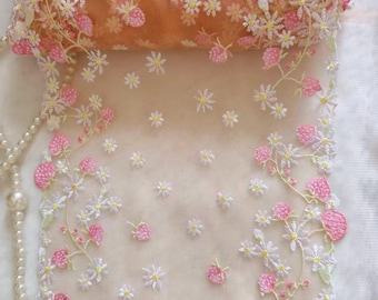 以下が含まれることがあります： 白いデイジーとピンクのイチゴのようなアクセントが刺繍された繊細なフローラルレース生地。 シアー素材はソフトピーチ色で、上部に丸められた部分があります。 左側には真珠のネックレスが見えます。