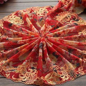 May include: Red sheer fabric with a gold floral embroidery trim. The fabric is folded in a fan shape, showcasing the intricate details of the embroidery.