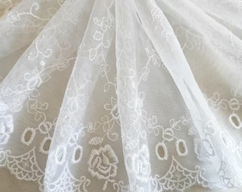 May include: Close-up of white lace fabric with floral and scalloped edge details. The delicate lace features embroidered flowers and openwork designs, creating a textured and elegant appearance. Ideal for bridal or craft projects.