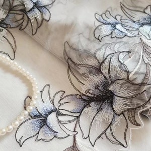 May include: White sheer fabric with embroidered floral designs in shades of gray and blue. The fabric has a delicate, airy feel and would be perfect for a variety of crafting projects.