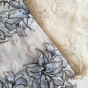 May include: Two pieces of white sheer fabric with embroidered floral designs. One piece has a white floral design and the other has a blue floral design.