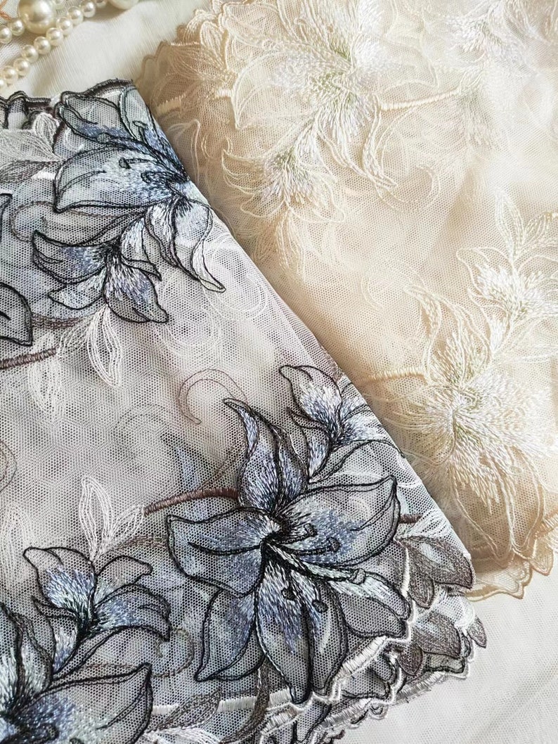 May include: Two pieces of white sheer fabric with embroidered floral designs. One piece has a white floral design and the other has a blue floral design.