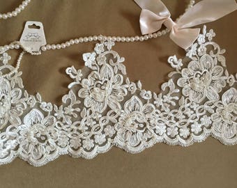Könnte beinhalten: Elfenbeinfarbene Spitzenborte mit einem gewellten Rand und Perlenbesatz. Die Spitze zeigt ein florales Design mit zarten Details.