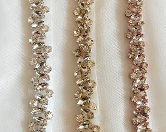 May include: Three strands of beaded trim with different colored metal settings. The trim is made of clear rhinestones in a marquise shape. The metal settings are silver, gold, and rose gold.