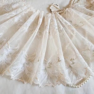 May include: Ivory white tulle lace trim with a delicate floral pattern. The lace has a scalloped edge and is perfect for adding a touch of elegance to any project.