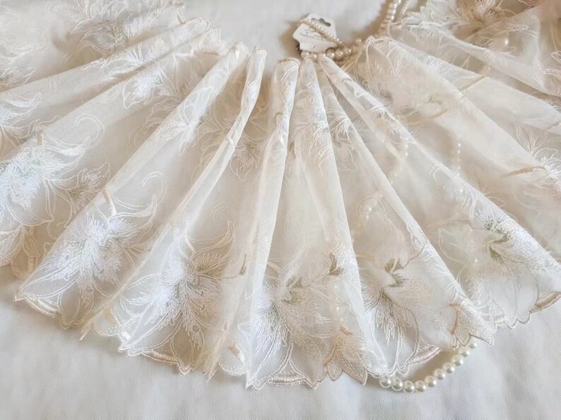 May include: Ivory white tulle lace trim with a delicate floral pattern. The lace has a scalloped edge and is perfect for adding a touch of elegance to any project.