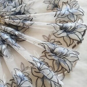 May include: White sheer fabric with a delicate floral embroidery design. The flowers are outlined in black and have a light blue center.