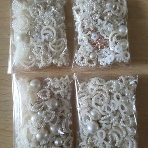 Könnte beinhalten: Vier durchsichtige Plastiktüten gefüllt mit weißen Perlen, weißen Perlenformen und weißen Perlenakzenten. Die Tüten befinden sich auf einer hellbraunen Holzoberfläche.