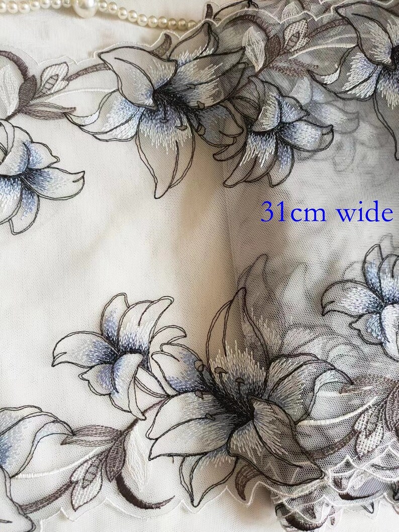May include: White sheer fabric with embroidered blue and brown lilies. The fabric is 31 inches wide.