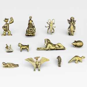 May include: A collection of small, gold-colored figurines. The figurines depict various subjects, including a strongman, a woman in a gown, an insect, an angel, a couple dancing, a dog, a sphinx, a mouse, a reclining figure, a pterodactyl, a soldier, and a dinosaur.