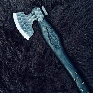 以下が含まれることがあります： 濃い青色の木製ハンドルと、質感のある銀色のヘッドを備えた手作りの斧。 斧の頭はハニカム模様です。 ハンドルには彫刻が施されており、小さな金属製のリベットで固定されています。