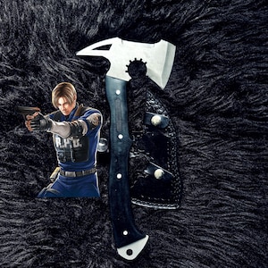 May include: A silver and black axe with a black handle and a leather sheath. The axe has a unique design with a pointed end and a gear-like detail. The image also features a character from a video game.