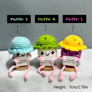 May include: Three crocheted muffin figures with hats, each holding a sign that reads "MUFFIN compares to you." The muffins are in blue, green, and yellow, with pink legs. The height is 2.76 inches.