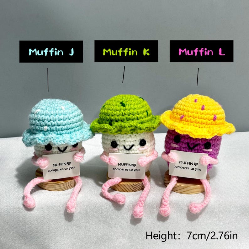 May include: Three crocheted muffin figures with hats, each holding a sign that reads "MUFFIN compares to you." The muffins are in blue, green, and yellow, with pink legs. The height is 2.76 inches.