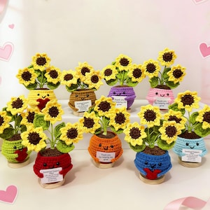 May include: A collection of handmade crochet sunflower plants in various colors, including yellow, red, orange, and blue. Each plant features a smiling face and a small sign with text. The sunflowers have yellow petals and brown centers.