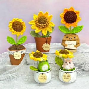 May include: A collection of handmade crochet sunflower decorations in small pots. The sunflowers are yellow and brown, with green leaves. Some pots have tags that read "Smile Everyday", "You are my sunshine", "Thank you for helping me grow", "Spread Sunshine", and "You are loved".