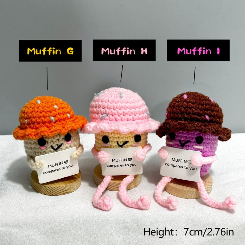 May include: Three crocheted muffin figures with hats, each holding a sign that reads "MUFFIN compares to you." The muffins are orange, pink, and brown, with black eyes and smiling faces. The height is 2.76 inches.
