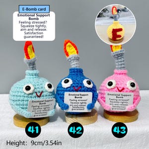 May include: Three handmade crochet "Emotional Support Bombs" in blue, pink, and blue-green, each with a gray fuse and a yellow and orange flame. Each bomb has googly eyes and a small sign. Height: 3.54 inches.