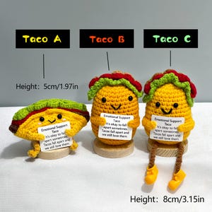 May include: Three crocheted taco toys, labeled Taco A, B, and C. Taco A is flat, while B and C are upright. Each has a smiling face and holds a sign that reads "Emotional Support Taco." Taco C is 8cm/3.15in tall.