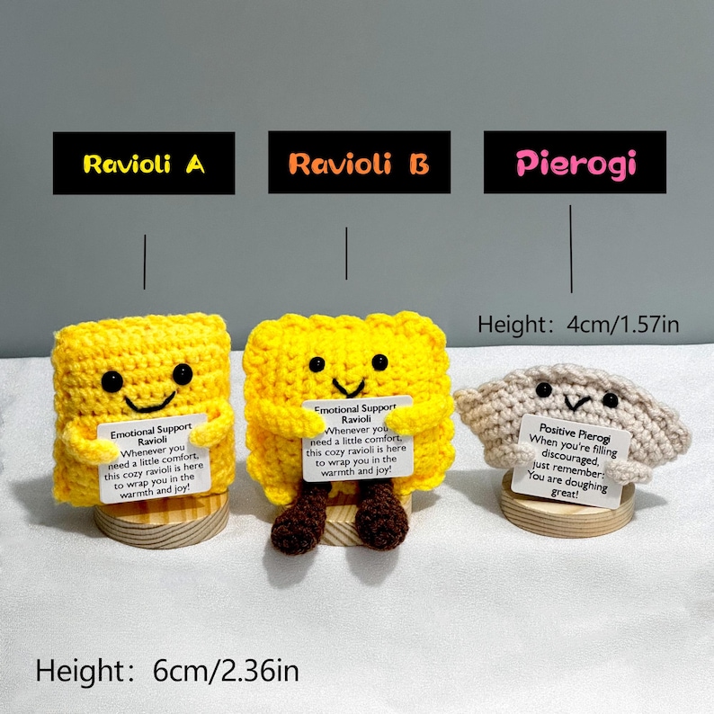 May include: Three handmade crochet food items: two yellow ravioli and one beige pierogi. The ravioli have smiling faces and the text "Emotional Support Ravioli." The pierogi has a smiling face and the text "Positive Pierogi." The ravioli are 6cm/2.36in tall, and the pierogi is 4cm/1.57in tall.