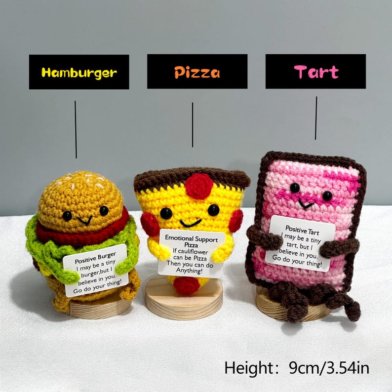 May include: Crocheted food-themed figurines, including a hamburger, pizza, and tart, each with a smiling face and a motivational message. The height of the figurines is 3.54 inches. The text on the signs reads "Positive Burger", "Emotional Support Pizza", and "Positive Tart".
