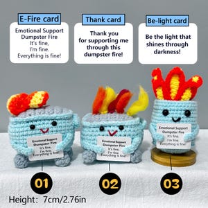 May include: Three crocheted dumpster fire figures, each with a unique flame design. The figures are light blue with smiling faces and hold small signs. The height is 2.76 inches.