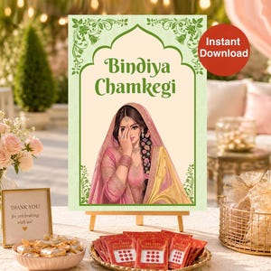 May include: A rectangular sign on a wooden easel featuring a green decorative border and the text Bindiya Chamkegi. The center displays an illustration of a person wearing a pink and yellow garment with a head covering, adorned with jewelry.