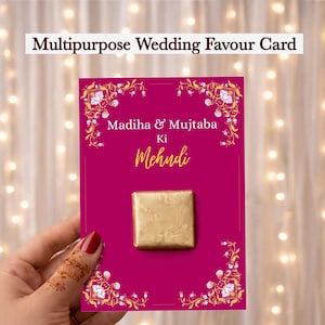 May include: A magenta wedding favor card with gold floral accents and text that reads "Multipurpose Wedding Favor Card." The card features the names "Madiha & Mujtaba" and "Ki Mehndi." A gold-wrapped square is attached.