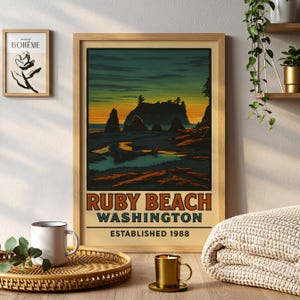 Könnte beinhalten: Ein gerahmter Druck von Ruby Beach, Washington, im Stil eines Vintage-Reiseposters. Das Kunstwerk zeigt einen Sonnenuntergang über dem Strand mit Felsformationen und dem Text "Ruby Beach Washington Established 1988". Der Rahmen ist aus hellem Holz.