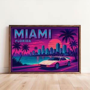 May include: A framed art print featuring a retro Miami, Florida scene. The artwork showcases a pink sports car driving along a coastal road, palm trees, and a cityscape under a vibrant sunset. The word "MIAMI" is displayed at the top.