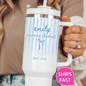 May include: White tumbler with blue vertical stripes and a handle. The tumbler has the name "emily" and the words "nursing student" in a script font, along with a bow graphic and the text "EST. 2026".