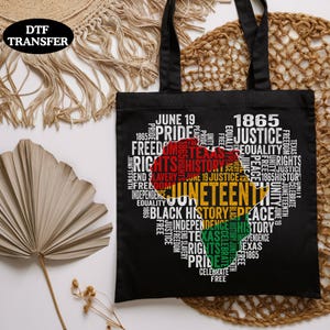 May include: Black tote bag with a heart-shaped design filled with words like "Juneteenth," "Freedom," and "Equality." The design incorporates the colors of the Juneteenth flag. The bag has black handles and the text "DTF TRANSFER" in the upper left corner.