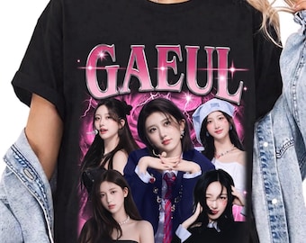Op de afbeelding: Een zwart t-shirt met korte mouwen en een grafische print van de naam GAEUL in grote roze letters bovenaan. Onder de tekst staan vijf fotografische portretten van een persoon in verschillende outfits tegen een felroze bliksemachtergrond.