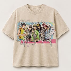 May include: A beige short-sleeve t-shirt featuring a graphic print of five stylized figures in various outfits. The design includes colorful accents, hand-drawn elements, and the text "CURTIS" in a casual font, set against a light blue rectangular background.
