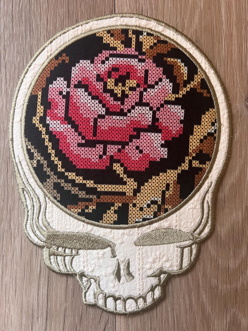 Peut inclure: &Eacute;cusson brod&eacute; repr&eacute;sentant un cr&acirc;ne stylis&eacute; avec une rose. La rose est de couleur rose et rouge sur fond noir. Le cr&acirc;ne est blanc avec des accents dor&eacute;s et marron. Un objet d&eacute;coratif unique.