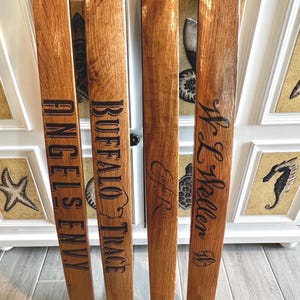 May include: Four reclaimed wood planks with dark lettering. The planks are engraved with the words "ANGELS ENVY", "BUFFALO TRACE", "E.H. Taylor", and "W.L. Weller". The wood has a natural, warm brown tone with visible grain.