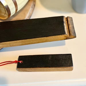 Puede incluir: Dos piezas rectangulares de madera con una parte superior oscura te&ntilde;ida y una base de madera m&aacute;s clara. Una pieza tiene una cuerda roja adjunta. La madera parece ser de un barril. Las piezas est&aacute;n sobre una superficie blanca.