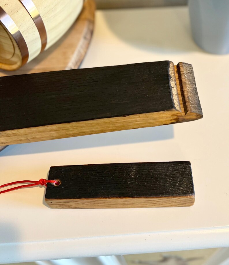 Puede incluir: Dos piezas rectangulares de madera con una parte superior oscura te&ntilde;ida y una base de madera m&aacute;s clara. Una pieza tiene una cuerda roja adjunta. La madera parece ser de un barril. Las piezas est&aacute;n sobre una superficie blanca.